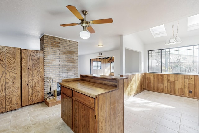 kitchen featuring a skylight, hanging light fixtures, kitchen peninsula, and wood walls