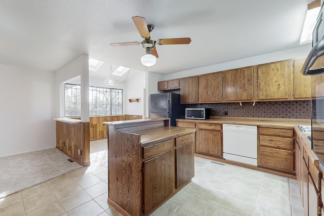 kitchen with dishwasher, backsplash, a center island, black fridge, and light carpet