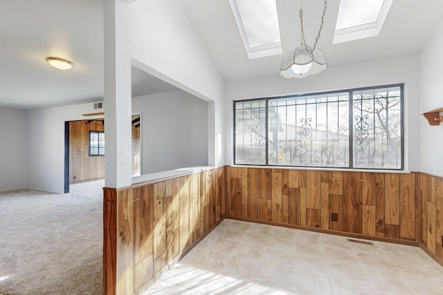 spare room featuring plenty of natural light, vaulted ceiling with skylight, and wood walls