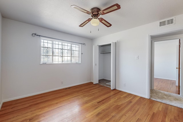 unfurnished bedroom featuring ceiling fan, a textured ceiling, a closet, and light wood-type flooring