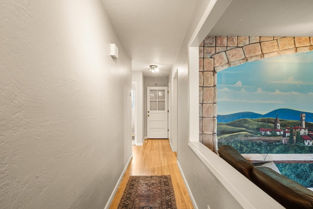 corridor with a textured wall, baseboards, and wood finished floors