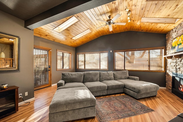 living room featuring lofted ceiling with skylight, wooden ceiling, light wood-type flooring, ceiling fan, and a fireplace