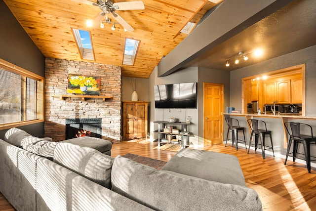 living room with wood ceiling, ceiling fan, vaulted ceiling with skylight, a stone fireplace, and light wood-type flooring