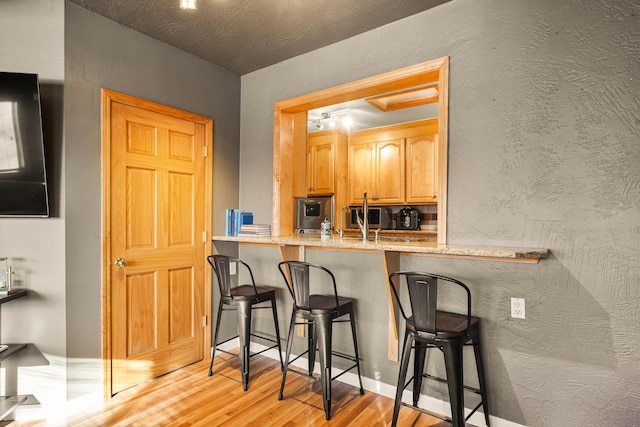 kitchen featuring light wood-style floors, a breakfast bar, and a textured wall