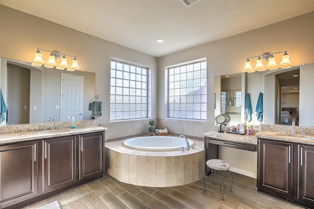 bathroom with vanity, a relaxing tiled tub, and a textured ceiling