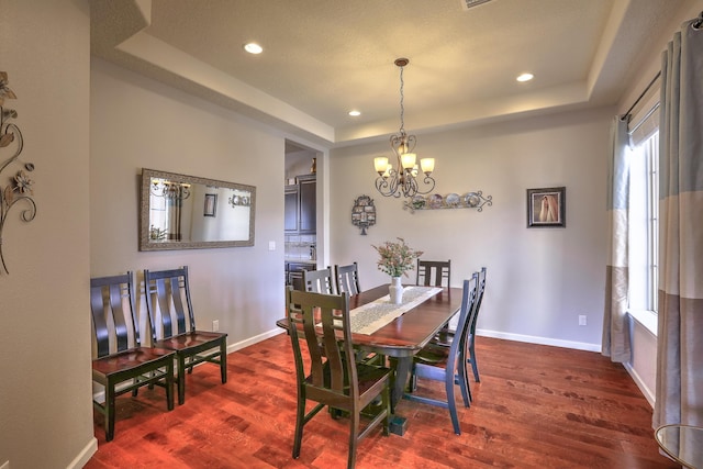 dining area featuring dark hardwood / wood-style floors, a raised ceiling, and a chandelier