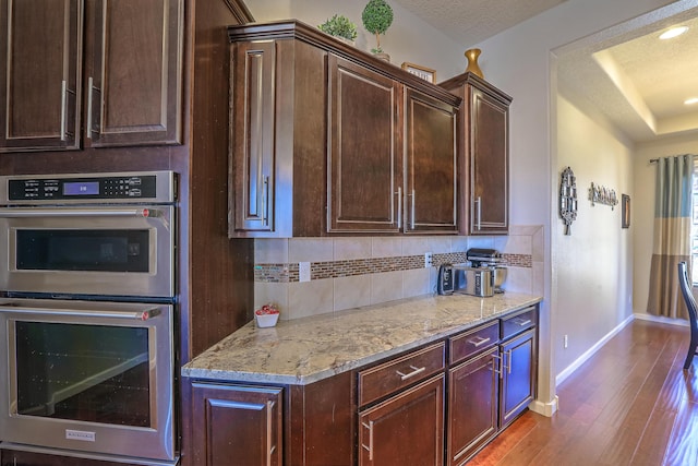 kitchen featuring light stone counters, tasteful backsplash, a textured ceiling, stainless steel double oven, and light hardwood / wood-style floors