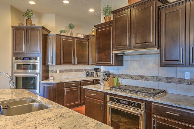 kitchen featuring sink, appliances with stainless steel finishes, dark brown cabinets, tasteful backsplash, and light stone countertops