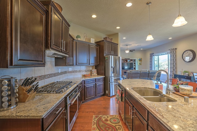 kitchen with dark brown cabinetry, sink, light stone counters, decorative light fixtures, and appliances with stainless steel finishes