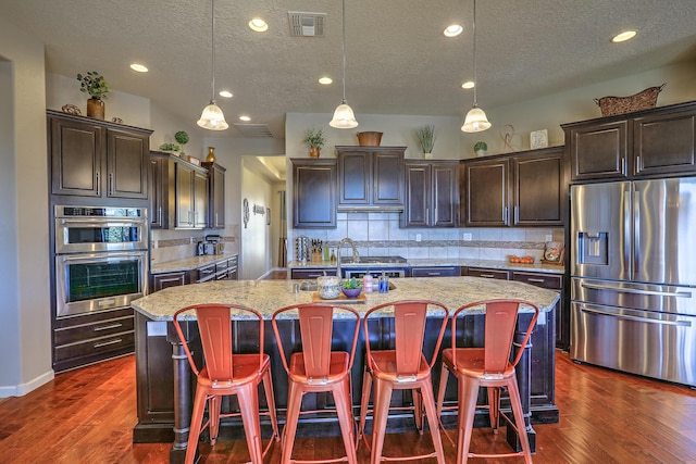 kitchen featuring sink, tasteful backsplash, hanging light fixtures, an island with sink, and stainless steel appliances