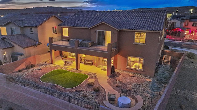 back house at dusk featuring an outdoor living space, a patio area, and a balcony