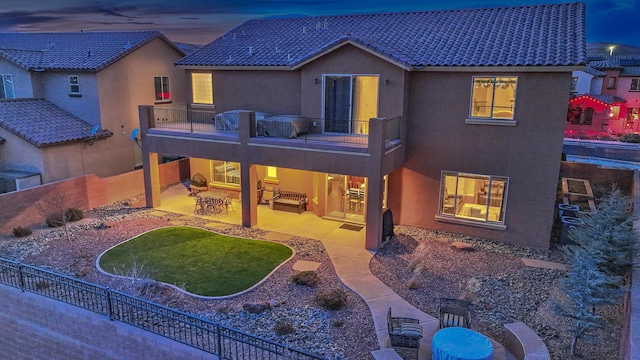 back house at dusk featuring a patio and a balcony