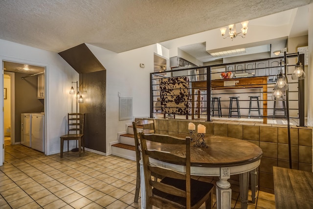 dining area featuring a notable chandelier, washer and clothes dryer, a textured ceiling, and light tile patterned floors