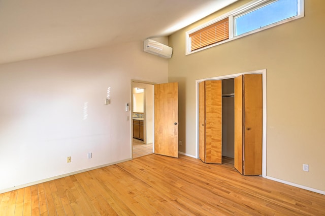 unfurnished bedroom with a closet, a wall mounted air conditioner, high vaulted ceiling, and light hardwood / wood-style flooring