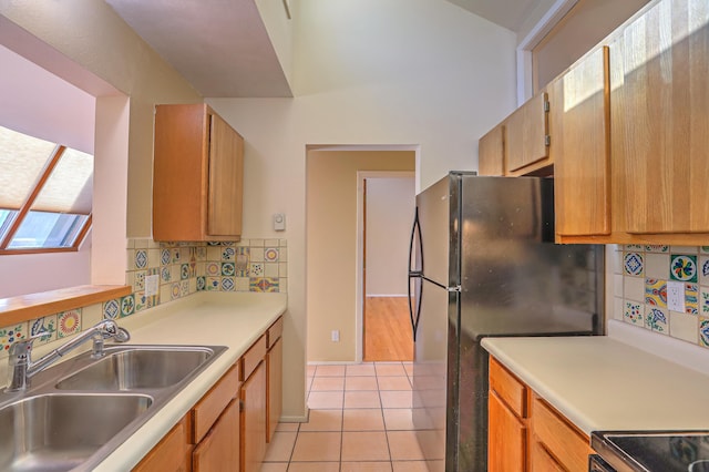 kitchen with electric stove, sink, light tile patterned floors, tasteful backsplash, and black fridge