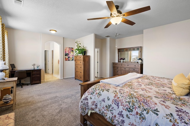 bedroom with light carpet, visible vents, arched walkways, a ceiling fan, and a textured ceiling