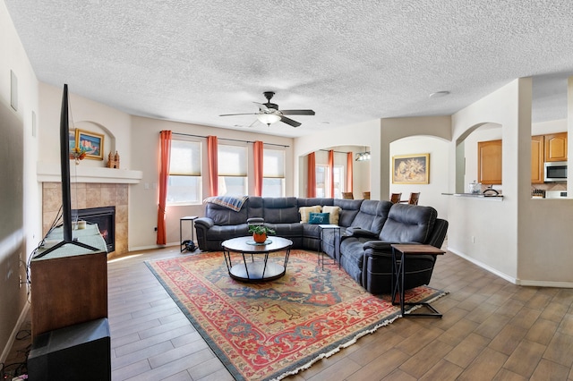 living area with dark wood-style floors, baseboards, arched walkways, and a tiled fireplace