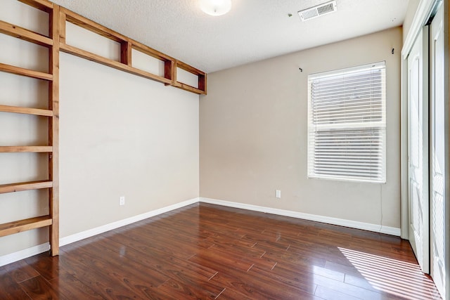 empty room with a textured ceiling and dark hardwood / wood-style flooring