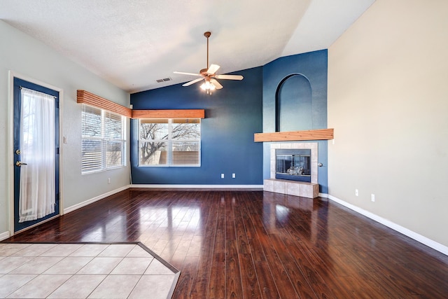 unfurnished living room with ceiling fan, lofted ceiling, a tiled fireplace, and hardwood / wood-style floors