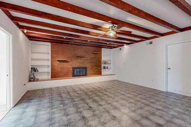 unfurnished living room featuring ceiling fan, beam ceiling, brick wall, a brick fireplace, and built in shelves