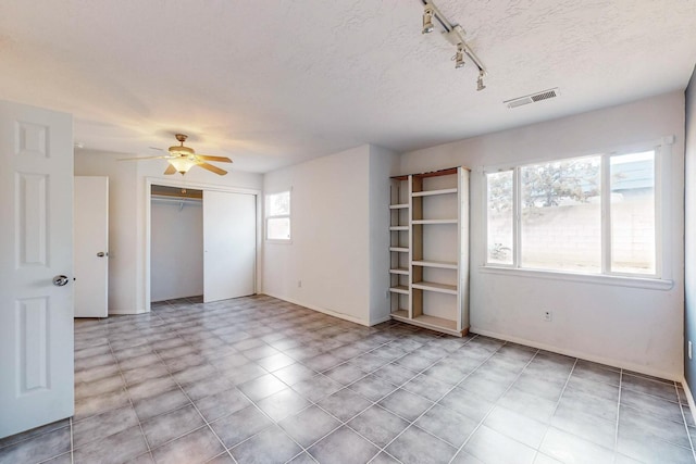 interior space with ceiling fan, rail lighting, a textured ceiling, and a closet