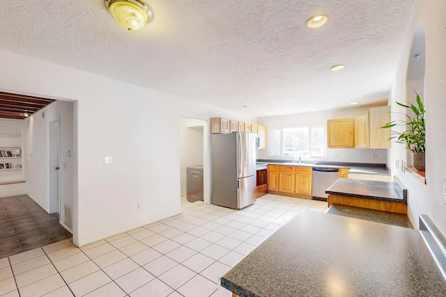 kitchen with light tile patterned flooring, appliances with stainless steel finishes, light brown cabinetry, sink, and a textured ceiling