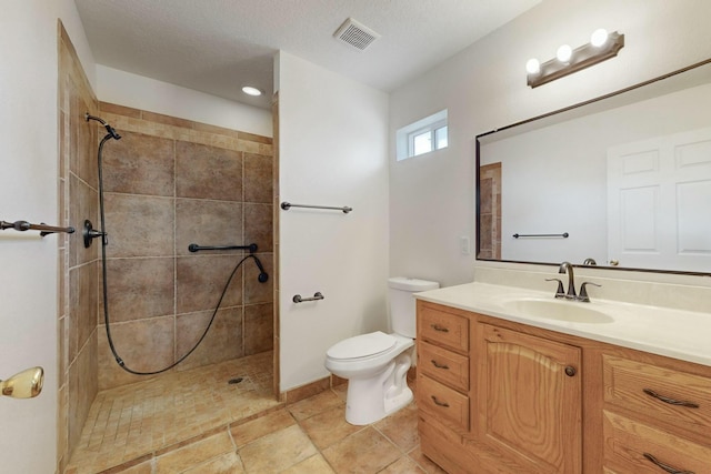 bathroom featuring vanity, toilet, a textured ceiling, and a tile shower