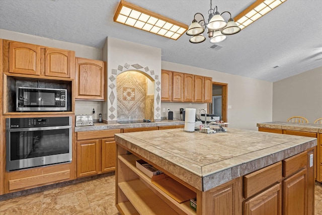 kitchen with a kitchen island, appliances with stainless steel finishes, pendant lighting, tile counters, and a notable chandelier