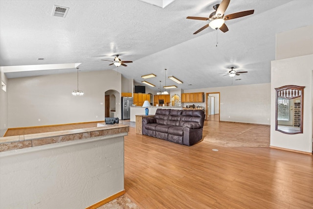 living room featuring vaulted ceiling, ceiling fan, light hardwood / wood-style floors, and a textured ceiling