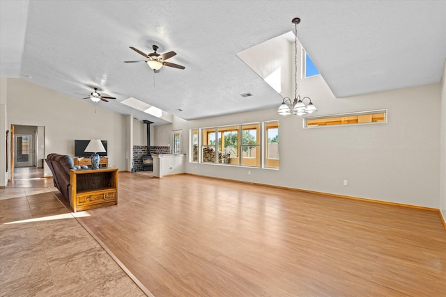 unfurnished living room featuring wood-type flooring, vaulted ceiling, a textured ceiling, a wood stove, and ceiling fan with notable chandelier