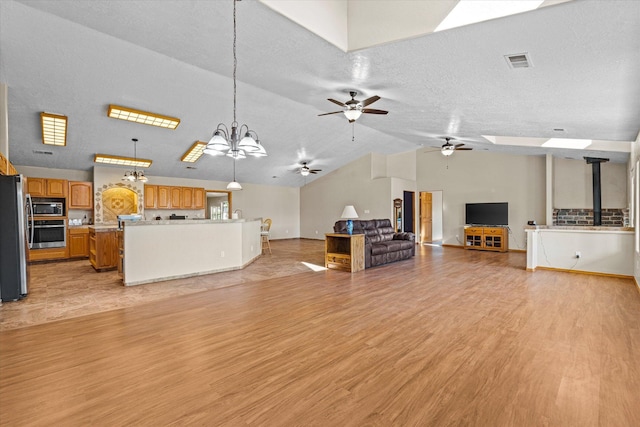 unfurnished living room featuring ceiling fan with notable chandelier, lofted ceiling with skylight, light hardwood / wood-style floors, and a textured ceiling