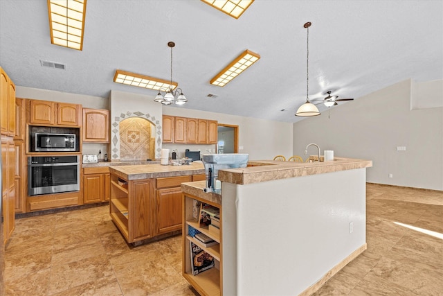 kitchen featuring built in microwave, an island with sink, hanging light fixtures, stainless steel oven, and ceiling fan