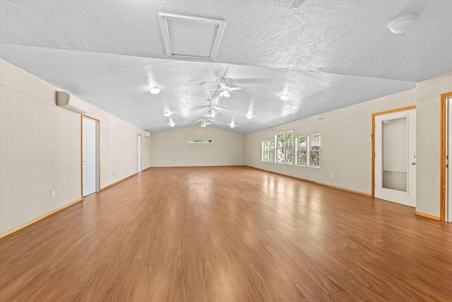 unfurnished living room with hardwood / wood-style floors, a textured ceiling, vaulted ceiling, and a wall mounted AC