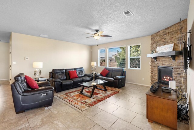 living room with a textured ceiling, a fireplace, ceiling fan, and light tile patterned flooring