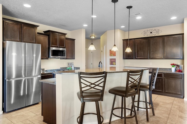 kitchen featuring pendant lighting, appliances with stainless steel finishes, a kitchen island with sink, and stone counters