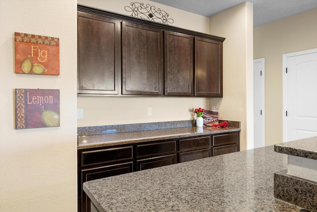 kitchen featuring light stone counters, dark brown cabinets, and a textured ceiling