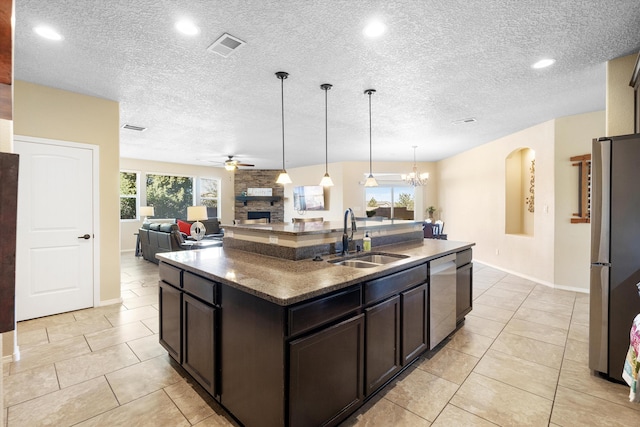 kitchen with appliances with stainless steel finishes, a stone fireplace, an island with sink, sink, and dark brown cabinets