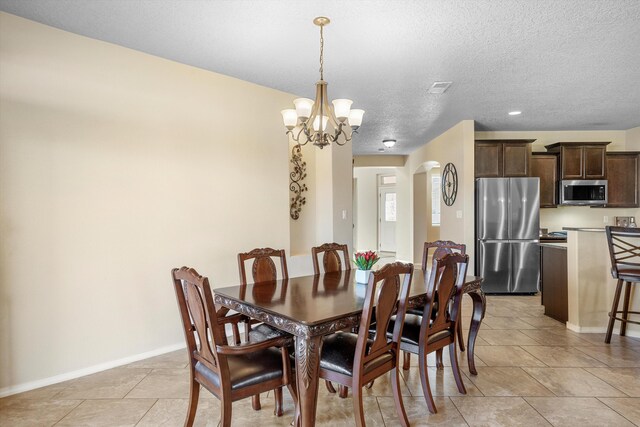 tiled dining space with a textured ceiling and a notable chandelier