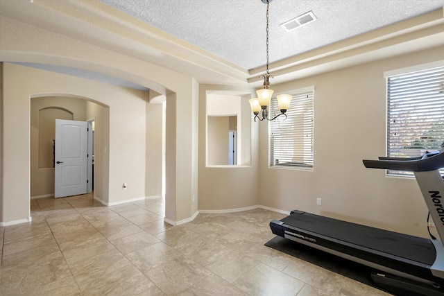 exercise room featuring a raised ceiling, a chandelier, a textured ceiling, and light tile patterned floors