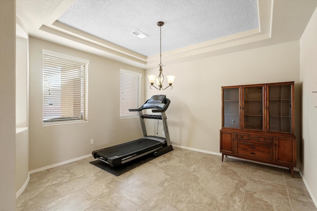 workout room featuring a tray ceiling, a textured ceiling, and a notable chandelier