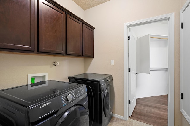 laundry area with cabinets, light hardwood / wood-style floors, washing machine and dryer, and a textured ceiling