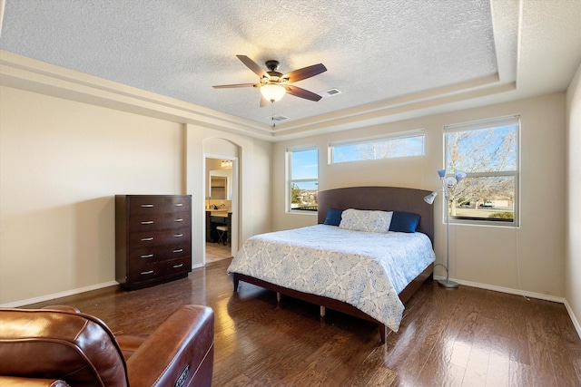 bedroom featuring ceiling fan, dark hardwood / wood-style floors, a textured ceiling, and a tray ceiling