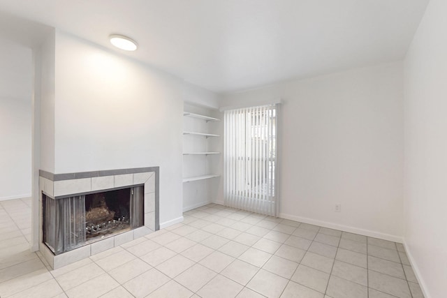 unfurnished living room with a tiled fireplace, light tile patterned flooring, and built in features