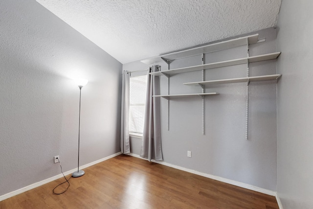 unfurnished bedroom featuring lofted ceiling, hardwood / wood-style floors, and a textured ceiling