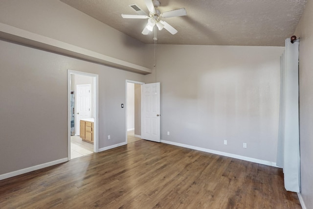 empty room featuring hardwood / wood-style flooring, ceiling fan, vaulted ceiling, and a textured ceiling