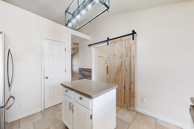 kitchen with white cabinetry, stainless steel fridge, a center island, light tile patterned floors, and a barn door