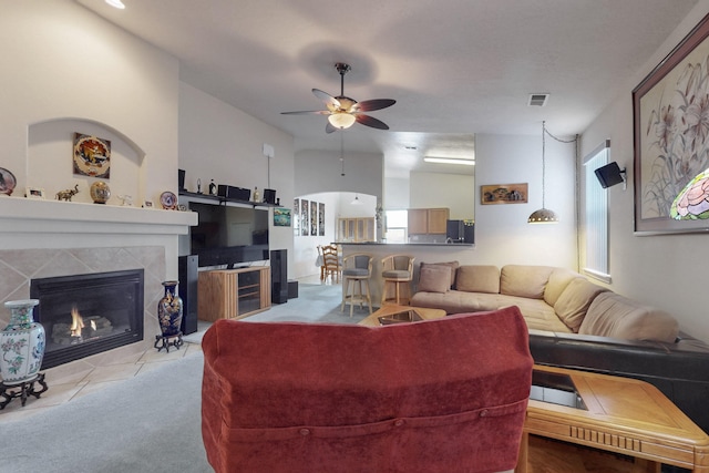 living room with a tiled fireplace, light colored carpet, and ceiling fan