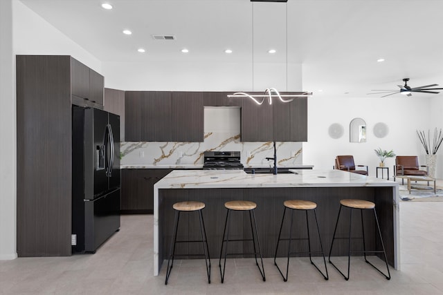 1145 15th St SE, Rio Rancho, NM 87124 - kitchen featuring a breakfast bar, hanging light fixtures, a kitchen island with sink, stainless steel range, and black fridge