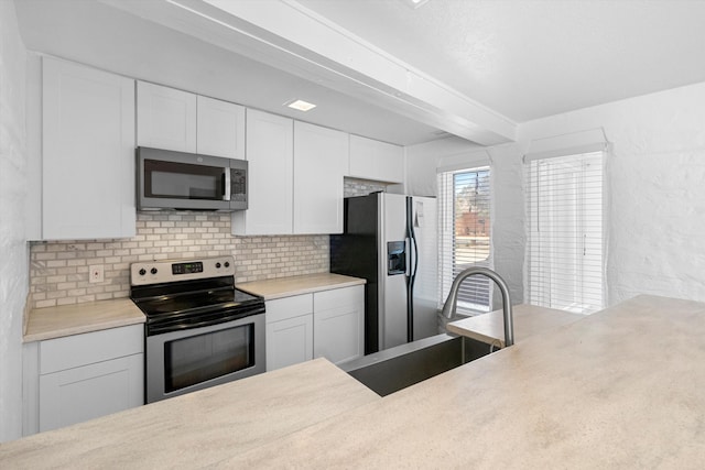 kitchen with appliances with stainless steel finishes, tasteful backsplash, white cabinetry, sink, and beam ceiling