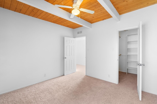 unfurnished bedroom with a spacious closet, light colored carpet, ceiling fan, wood ceiling, and beam ceiling